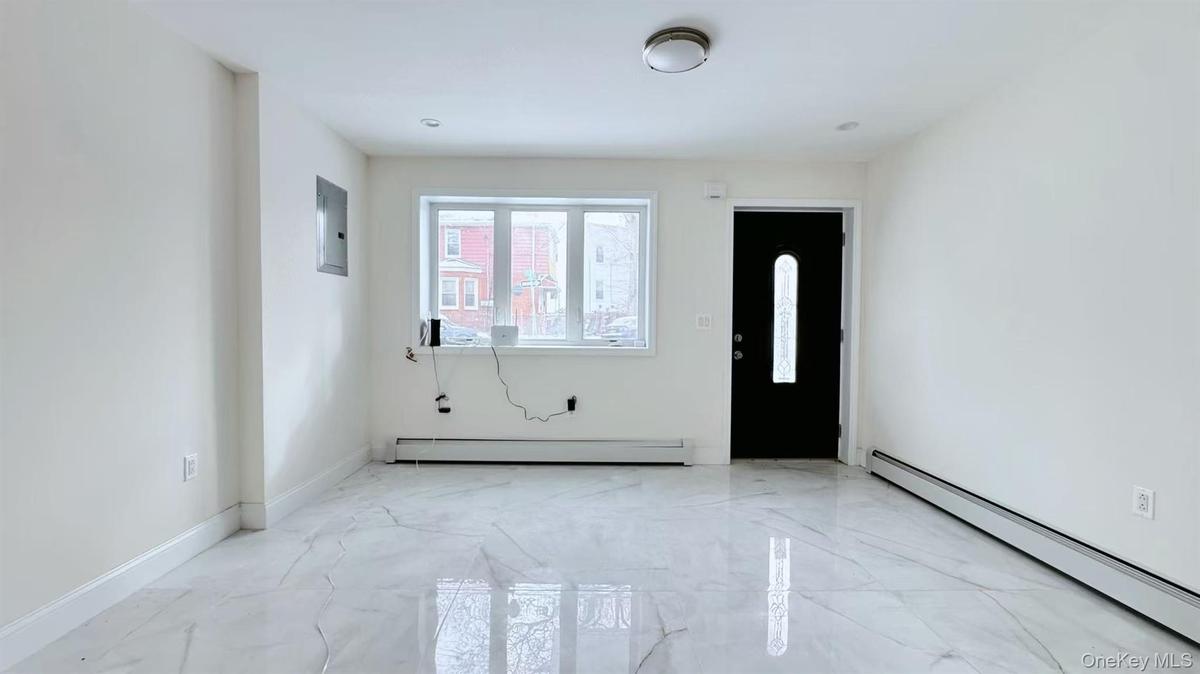 Spare room featuring a baseboard heating unit, light marble finish flooring, and electric panel