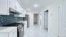 Kitchen featuring stainless steel appliances, white cabinets, under cabinet range hood, light stone countertops, and light marble finish floors