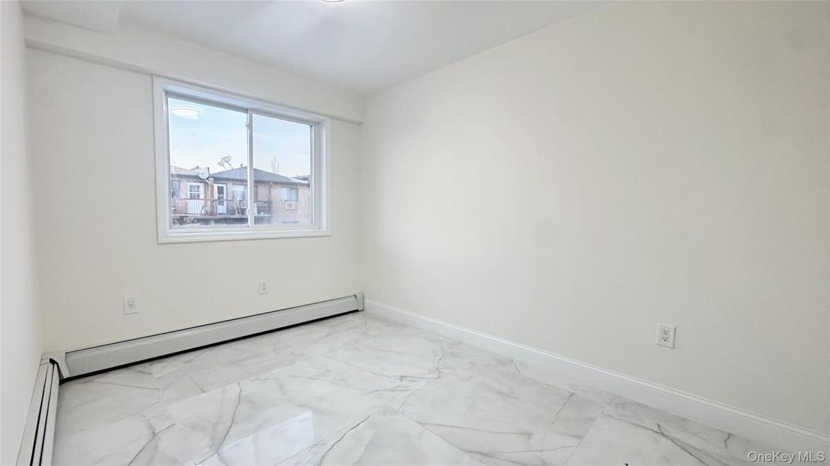 Unfurnished room featuring light marble finish floors and a baseboard heating unit