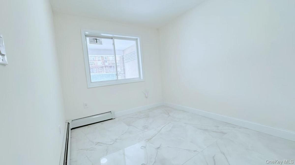 Unfurnished room featuring light marble finish floors and a baseboard radiator
