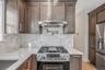 Kitchen with appliances with stainless steel finishes, light stone counters, exhaust hood, tasteful backsplash, and light wood-type flooring. For Mark