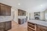 Kitchen featuring light stone countertops, dark brown cabinets, backsplash, a stone fireplace, and light wood finished floors. For Marketing Purposes!