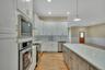 Kitchen featuring a wainscoted wall, appliances with stainless steel finishes, light wood-type flooring, light stone countertops, and hanging light fi