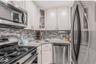 Kitchen with appliances with stainless steel finishes, glass insert cabinets, light stone countertops, white cabinets, and decorative backsplash