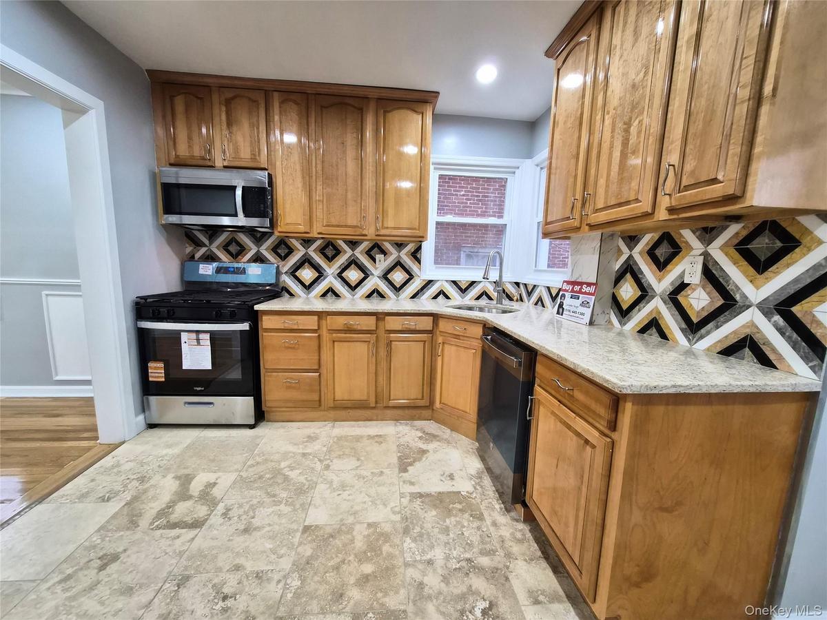 Kitchen featuring appliances with stainless steel finishes, brown cabinetry, light stone counters, and backsplash