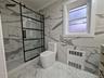 Full bath with light marble finish flooring, a marble finish shower, vanity, radiator, and tile walls