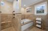 Bathroom with tile walls, healthy amount of natural light, a wainscoted wall, a garden tub, and crown molding