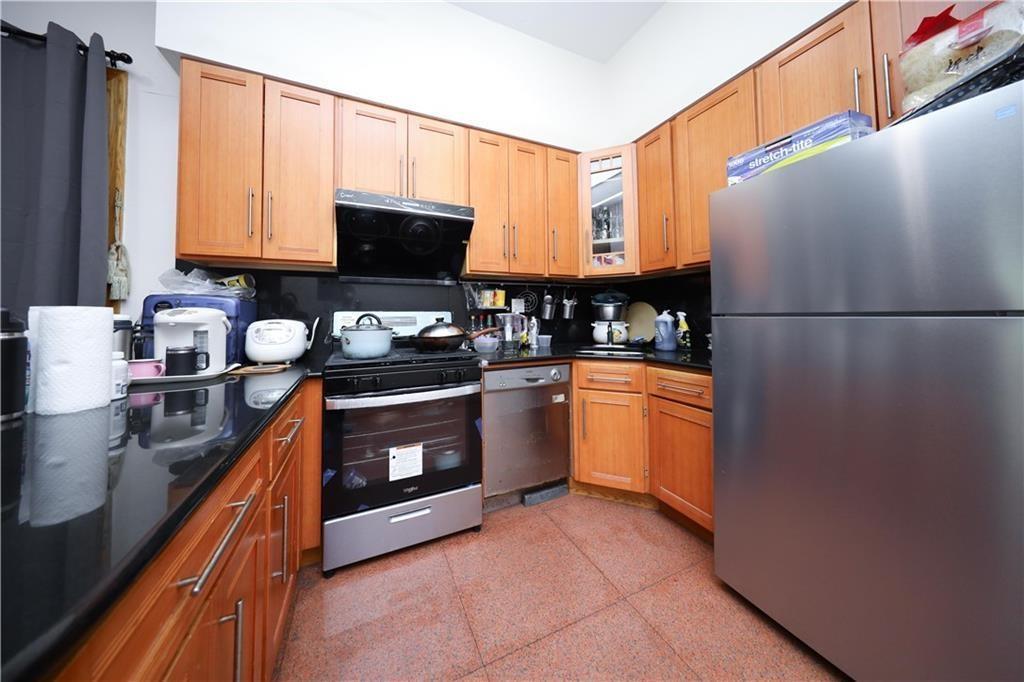 Kitchen featuring appliances with stainless steel finishes, dark aggregate flooring, extractor fan, glass insert cabinets, and brown cabinets