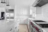 Kitchen featuring high quality appliances, ventilation hood, white cabinets, wooden ceiling, and light stone counters