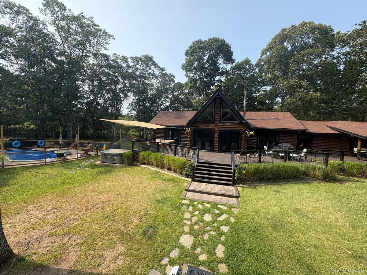 Rear view of house featuring an outdoor pool, a patio, faux log siding, and view of scattered trees