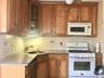 Kitchen featuring white appliances, brown cabinetry, glass insert cabinets, dark stone counters, and tasteful backsplash