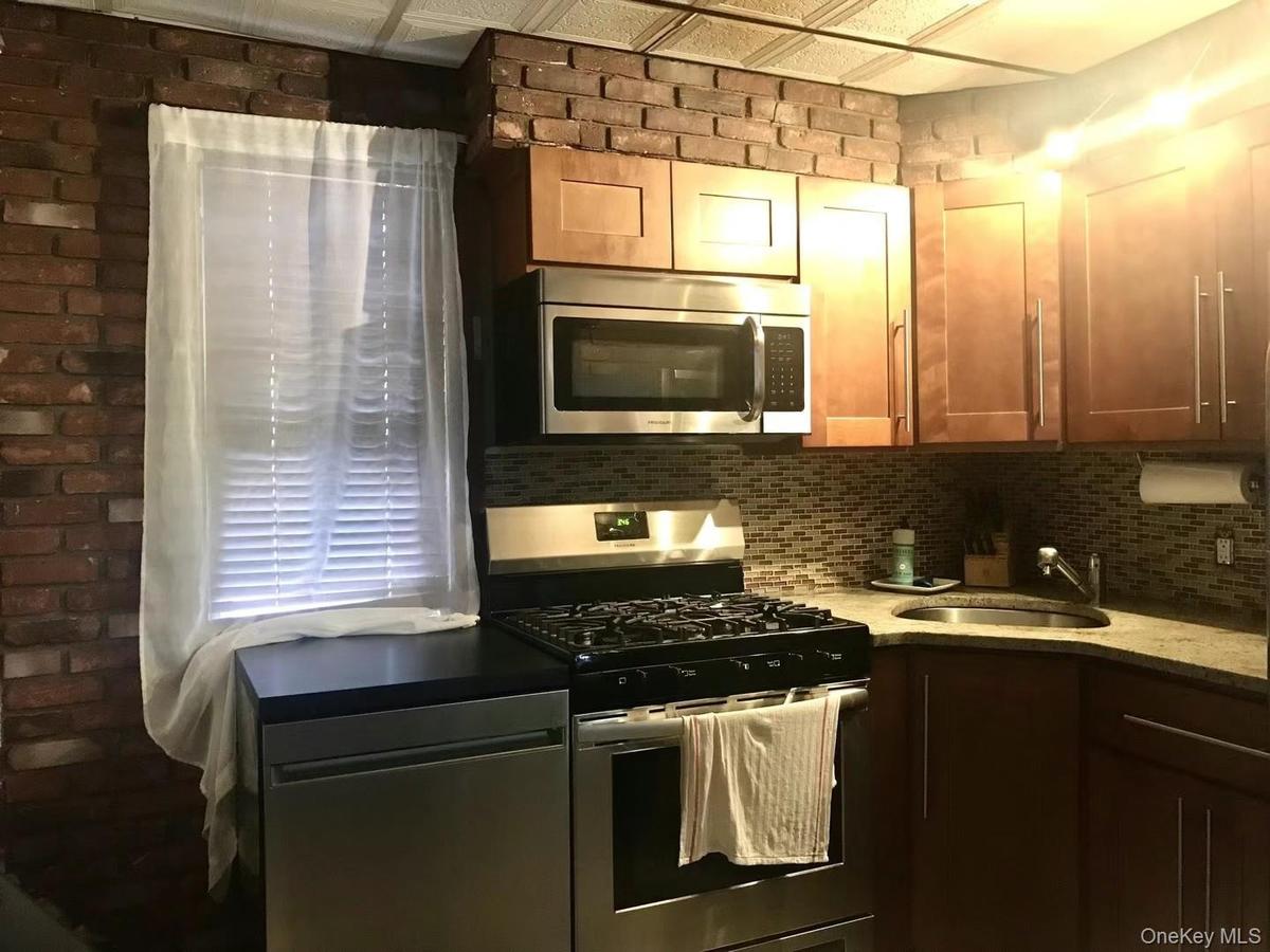 Kitchen featuring stainless steel appliances, tasteful backsplash, dark stone counters, and brick wall