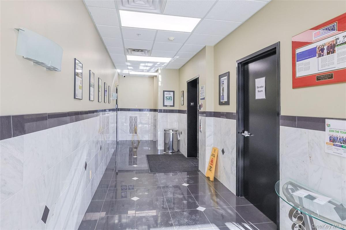 Corridor with a paneled ceiling, dark tile patterned floors, tile walls, elevator, and wainscoting
