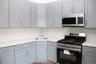 Kitchen with appliances with stainless steel finishes, gray cabinets, light stone counters, and backsplash