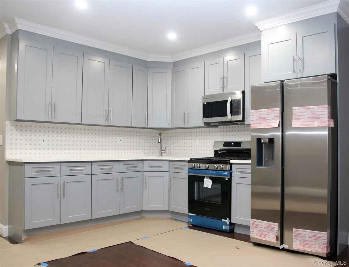Kitchen with stainless steel appliances, crown molding, light stone countertops, and gray cabinets