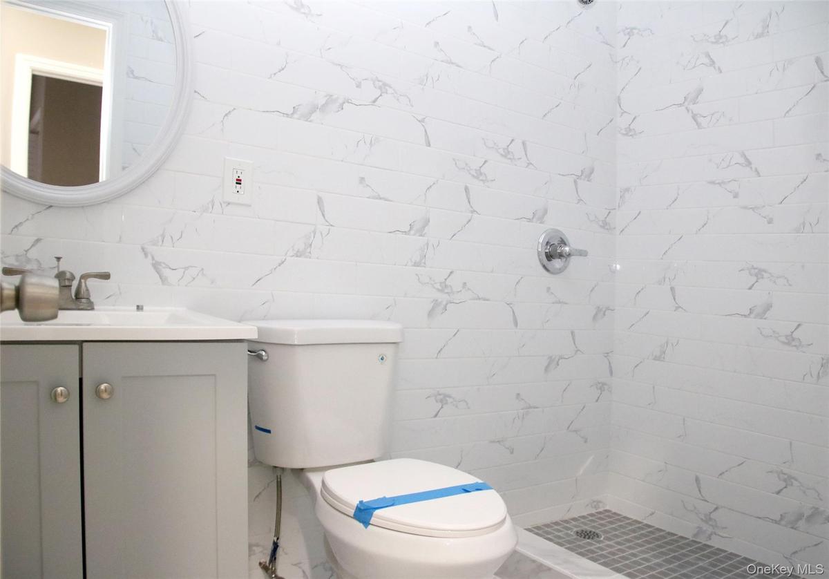 Full bathroom with tile walls, vanity, a tile shower, and marble look tile flooring