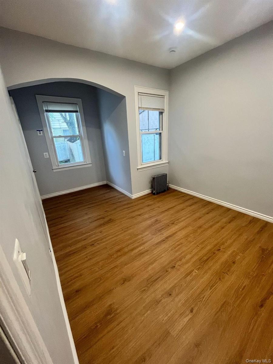 Unfurnished room featuring wood finished floors, radiator heating unit, and arched walkways