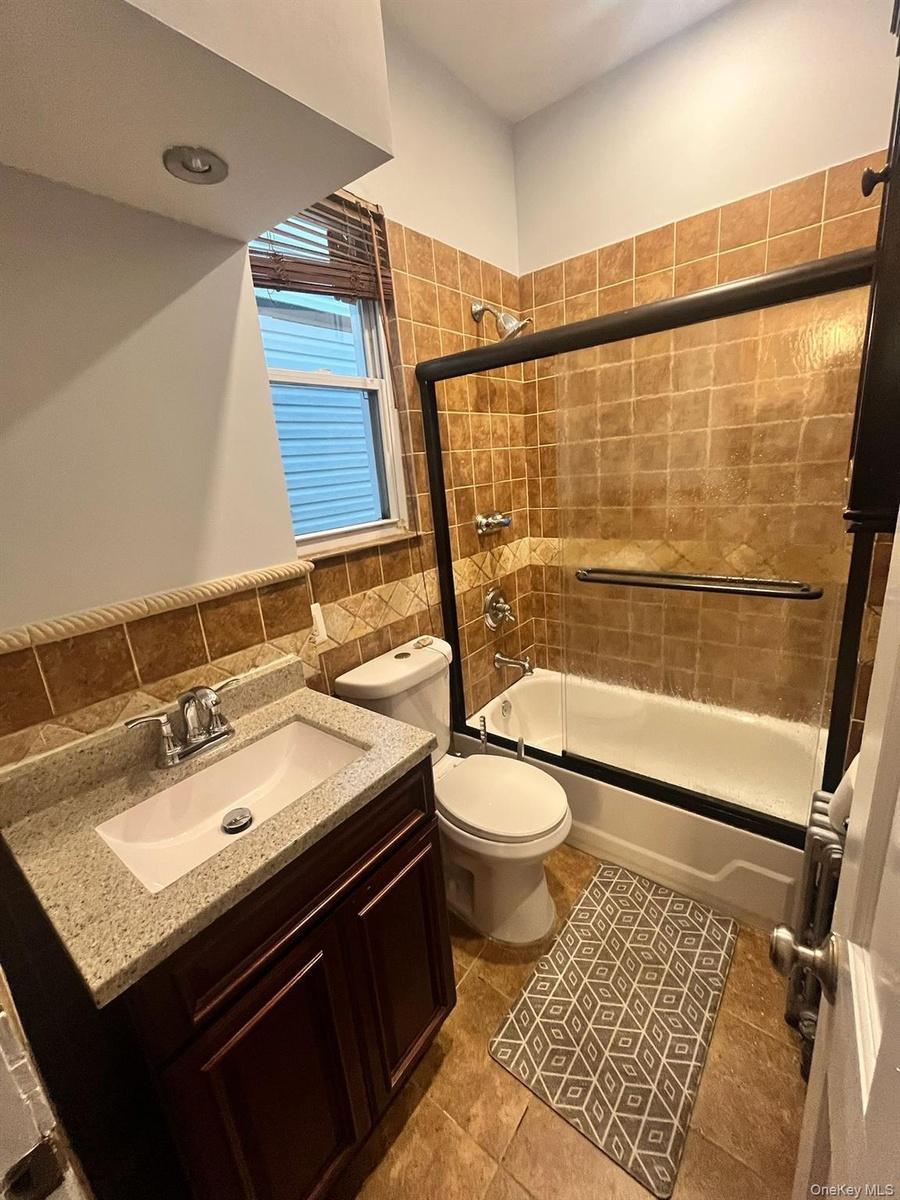 Bathroom with vanity, shower / bath combination with glass door, tile walls, and dark tile patterned flooring