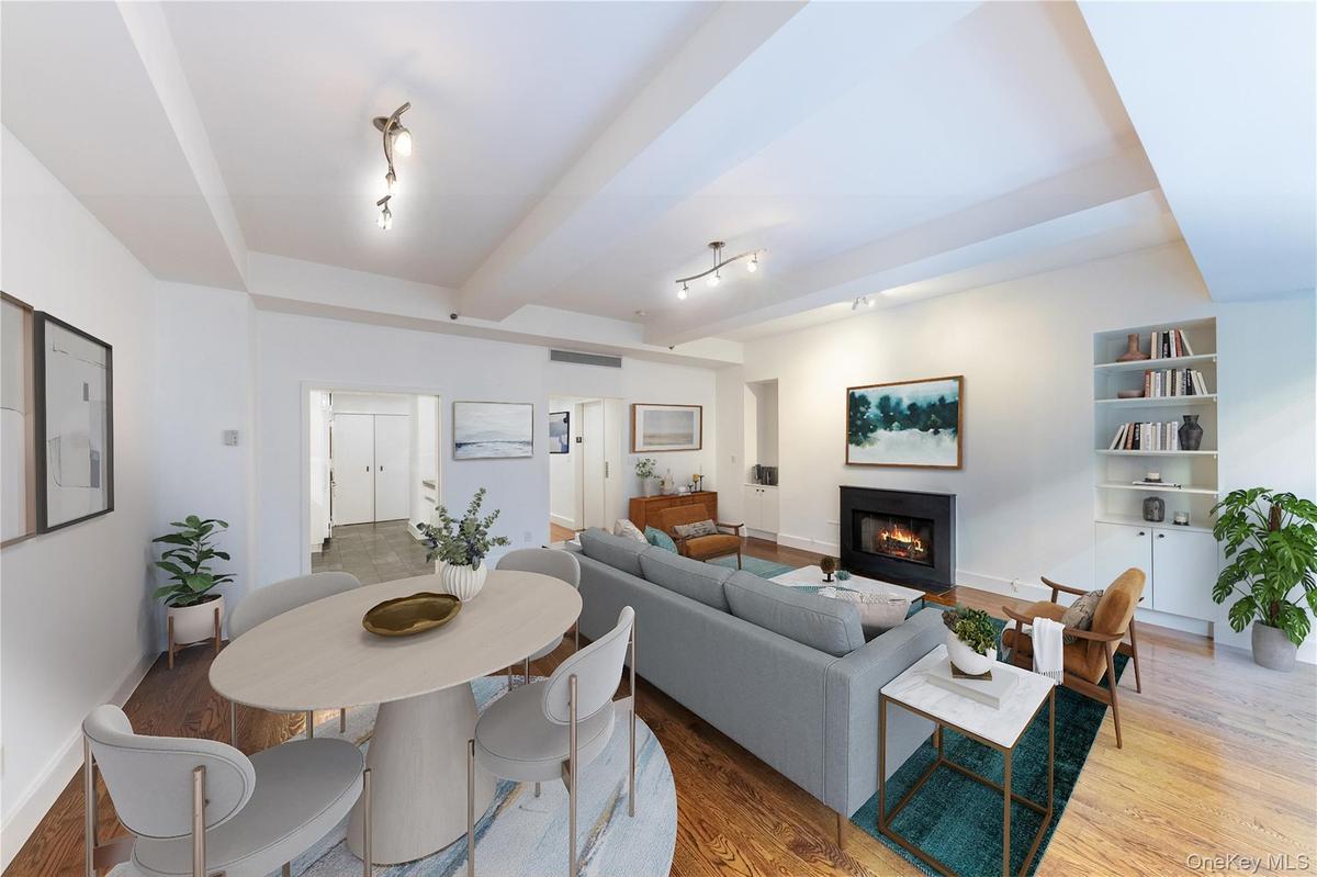 Living area featuring light wood-style flooring, a warm lit fireplace, beamed ceiling, built in features, and track lighting
