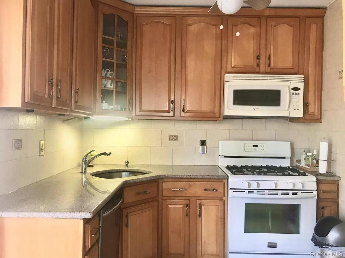 Kitchen featuring white appliances, brown cabinetry, glass insert cabinets, dark stone counters, and tasteful backsplash