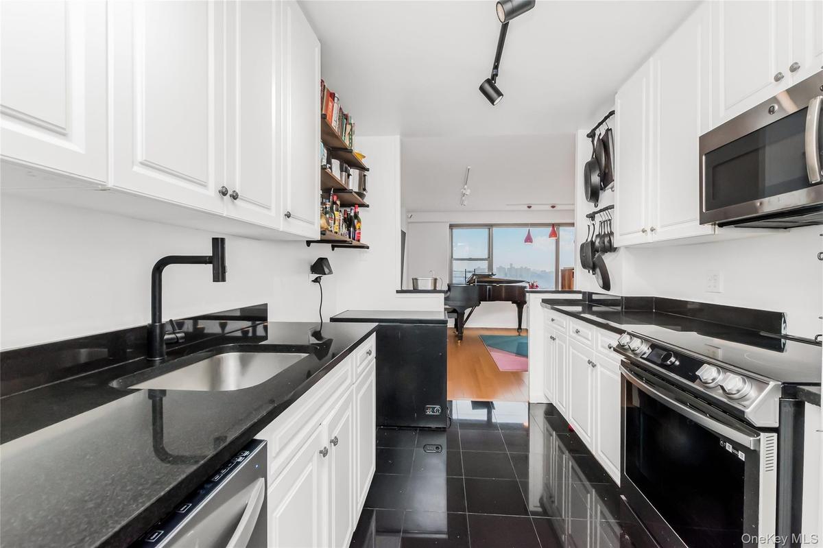 Kitchen with stainless steel appliances, white cabinetry, open shelves, dark stone counters, and rail lighting