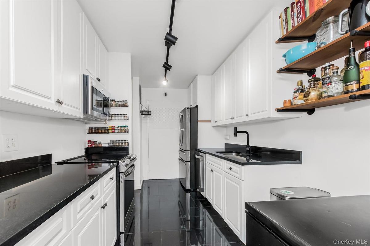 Kitchen with stainless steel appliances, track lighting, white cabinetry, and open shelves