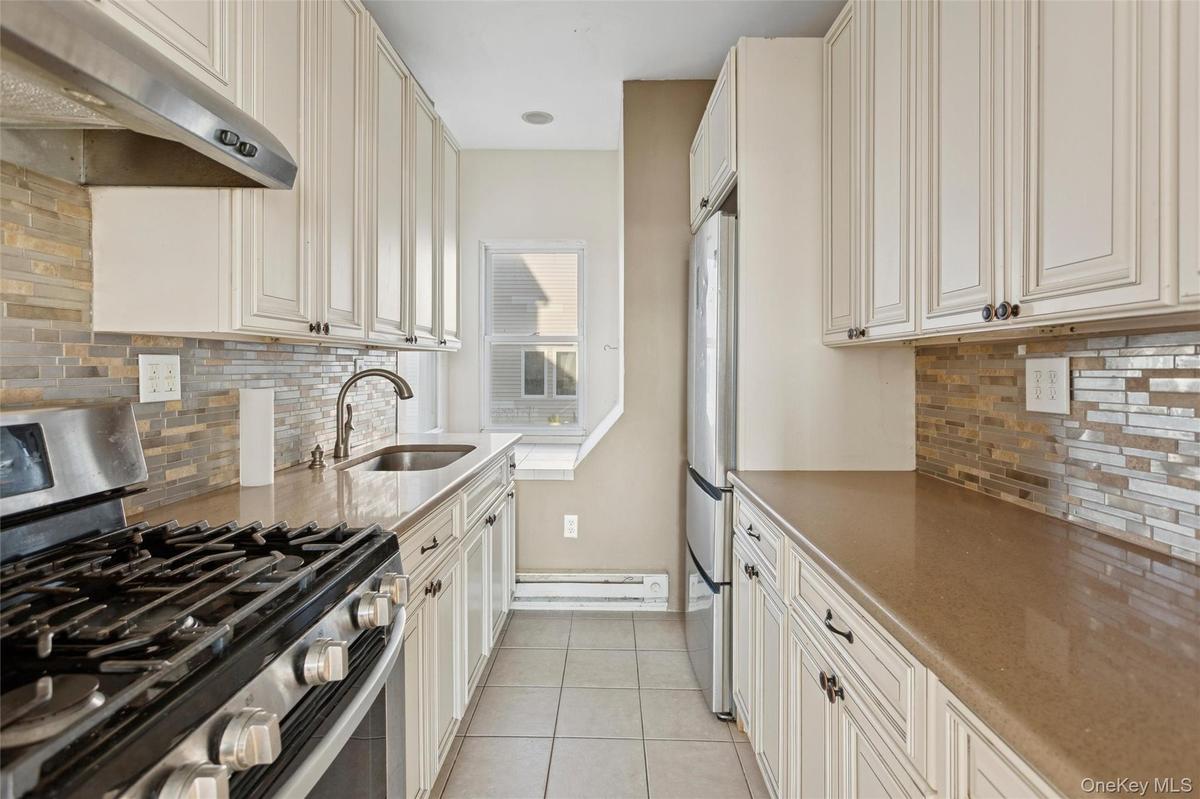 Kitchen with appliances with stainless steel finishes, under cabinet range hood, light stone counters, and light tile patterned flooring
