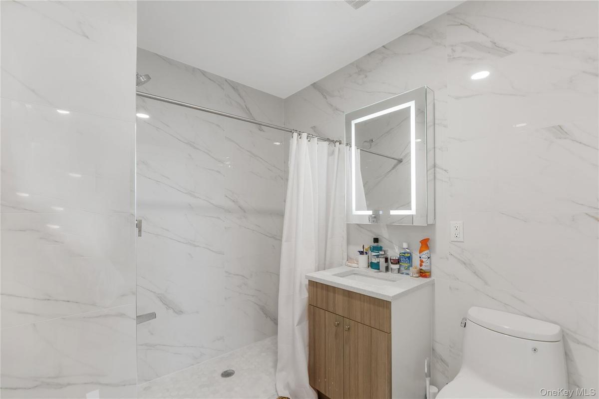 Bathroom featuring vanity, a marble finish shower, and stone wall