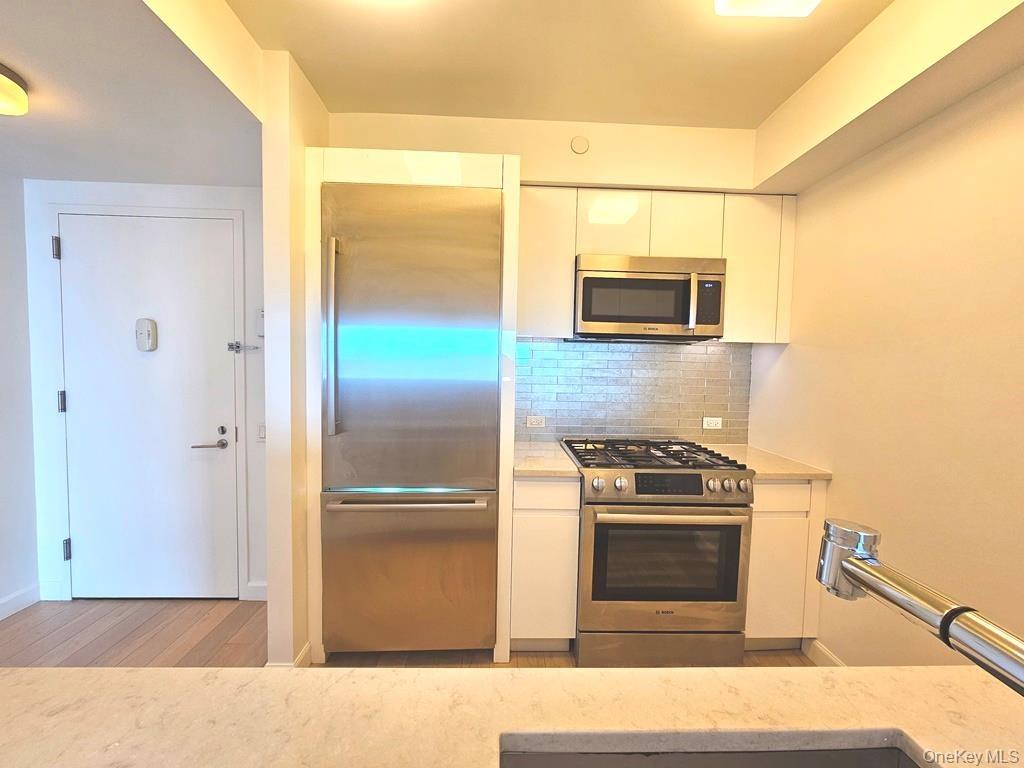 Kitchen featuring white cabinetry, appliances with stainless steel finishes, backsplash, light stone countertops, and modern cabinets