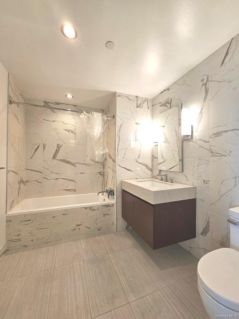 Bathroom featuring tile walls, vanity, and a combined bath / shower with marble appearance