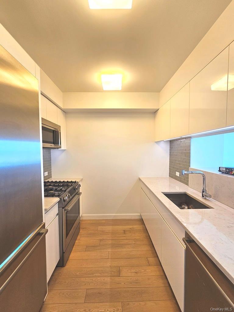 Kitchen featuring modern cabinets, white cabinetry, stainless steel appliances, and light stone counters