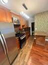 Kitchen with stainless steel appliances, dark stone countertops, brown cabinets, hanging light fixtures, and light wood finished floors