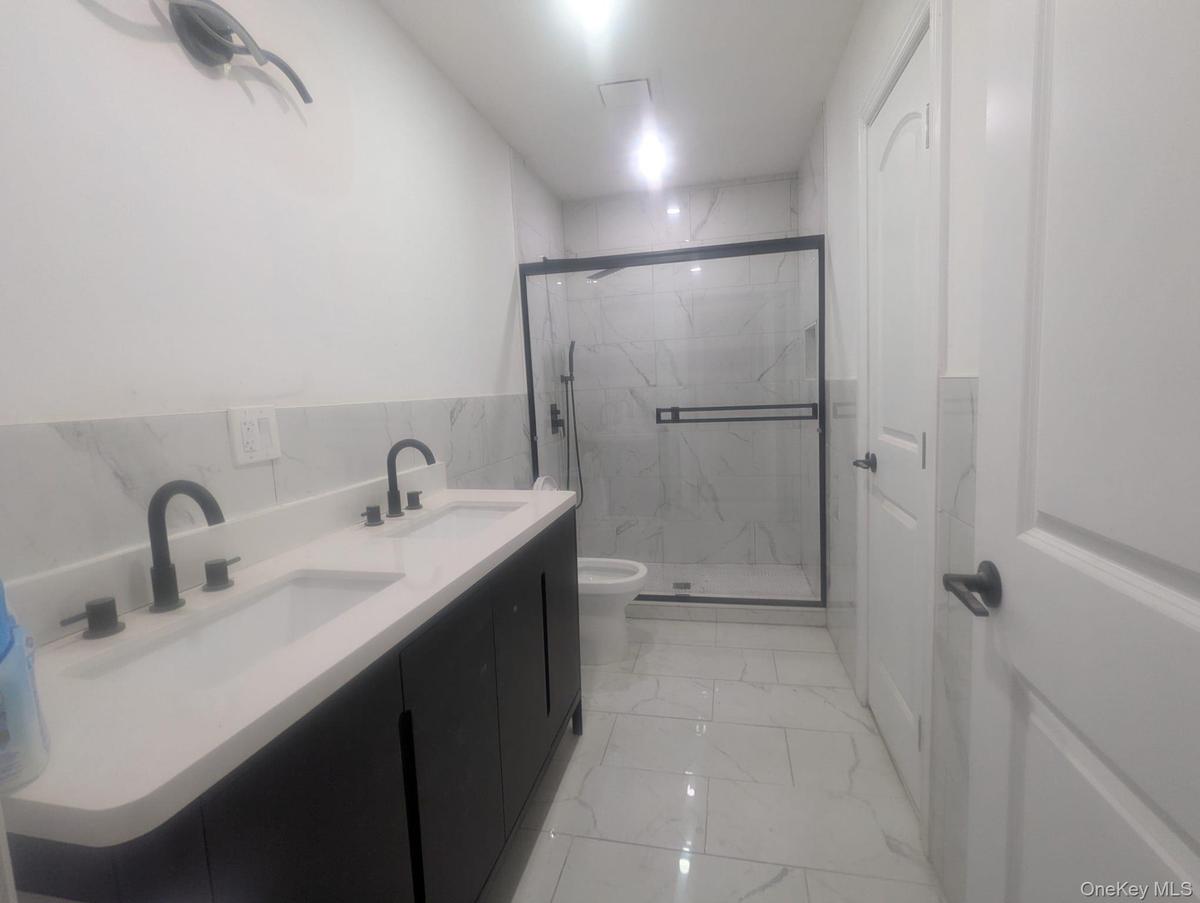 Bathroom with double vanity, a marble finish shower, light marble finish flooring, tile walls, and wainscoting