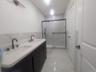 Bathroom with double vanity, a marble finish shower, light marble finish flooring, tile walls, and wainscoting