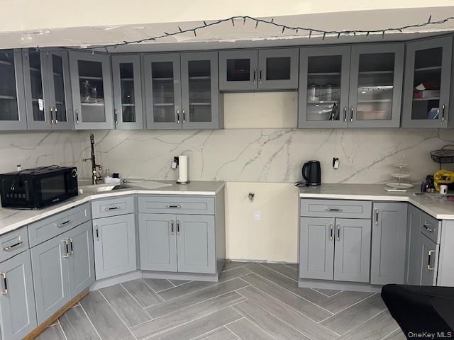 Kitchen with gray cabinetry, glass insert cabinets, black microwave, and backsplash