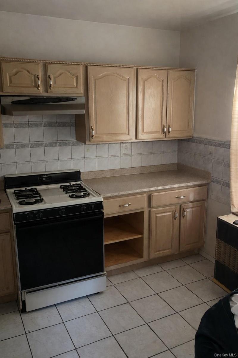 Kitchen with gas stove, light countertops, light tile patterned flooring, under cabinet range hood, and tile walls