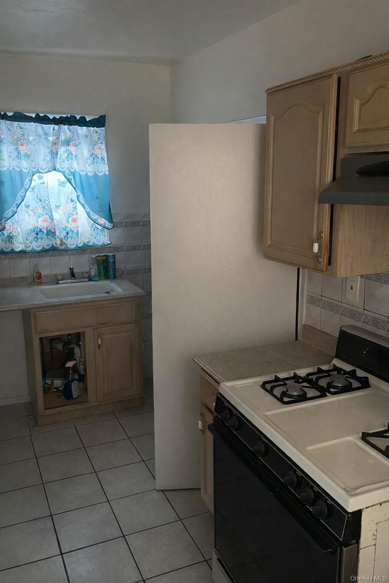 Kitchen with white range with gas cooktop, light countertops, under cabinet range hood, light tile patterned floors, and light brown cabinetry