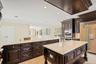 Kitchen with dark brown cabinetry, exhaust hood, paneled built in fridge, light stone countertops, and stainless steel double oven