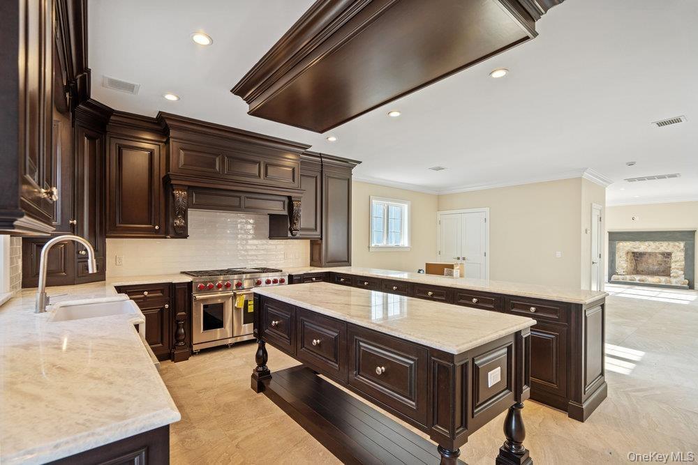Kitchen with dark brown cabinetry, a peninsula, open floor plan, double oven range, and crown molding