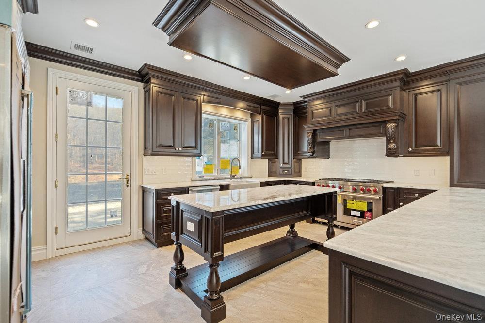 Kitchen with dark brown cabinetry, backsplash, crown molding, and recessed lighting