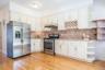 Kitchen with open shelves, appliances with stainless steel finishes, under cabinet range hood, light stone counters, and light wood-style flooring