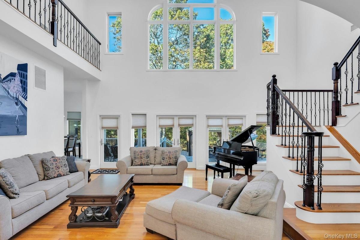 Living room with stairs, light wood finished floors, and a high ceiling