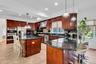 Kitchen with a kitchen breakfast bar, dark stone countertops, decorative light fixtures, backsplash, and a kitchen island with sink