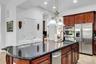 Kitchen with dark stone counters, light tile patterned flooring, stainless steel fridge with ice dispenser, an island with sink, and hanging light fix