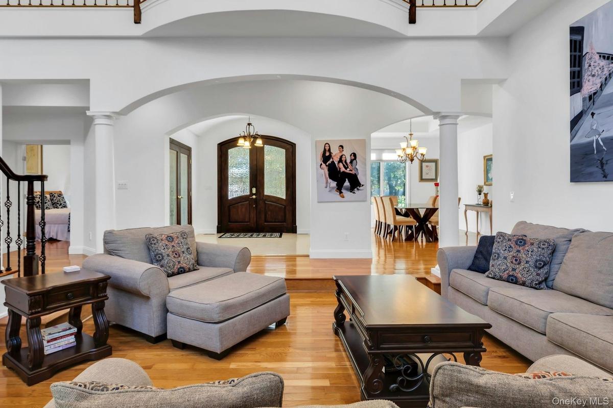 Living area with a chandelier, hardwood / wood-style floors, stairway, ornate columns, and a towering ceiling