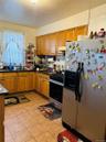 Kitchen featuring appliances with stainless steel finishes, brown cabinetry, decorative backsplash, light tile patterned flooring, and dark stone coun