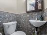 Half bathroom featuring wallpapered walls and wainscoting