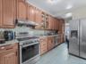 Kitchen with stainless steel appliances, under cabinet range hood, backsplash, glass insert cabinets, and light stone countertops