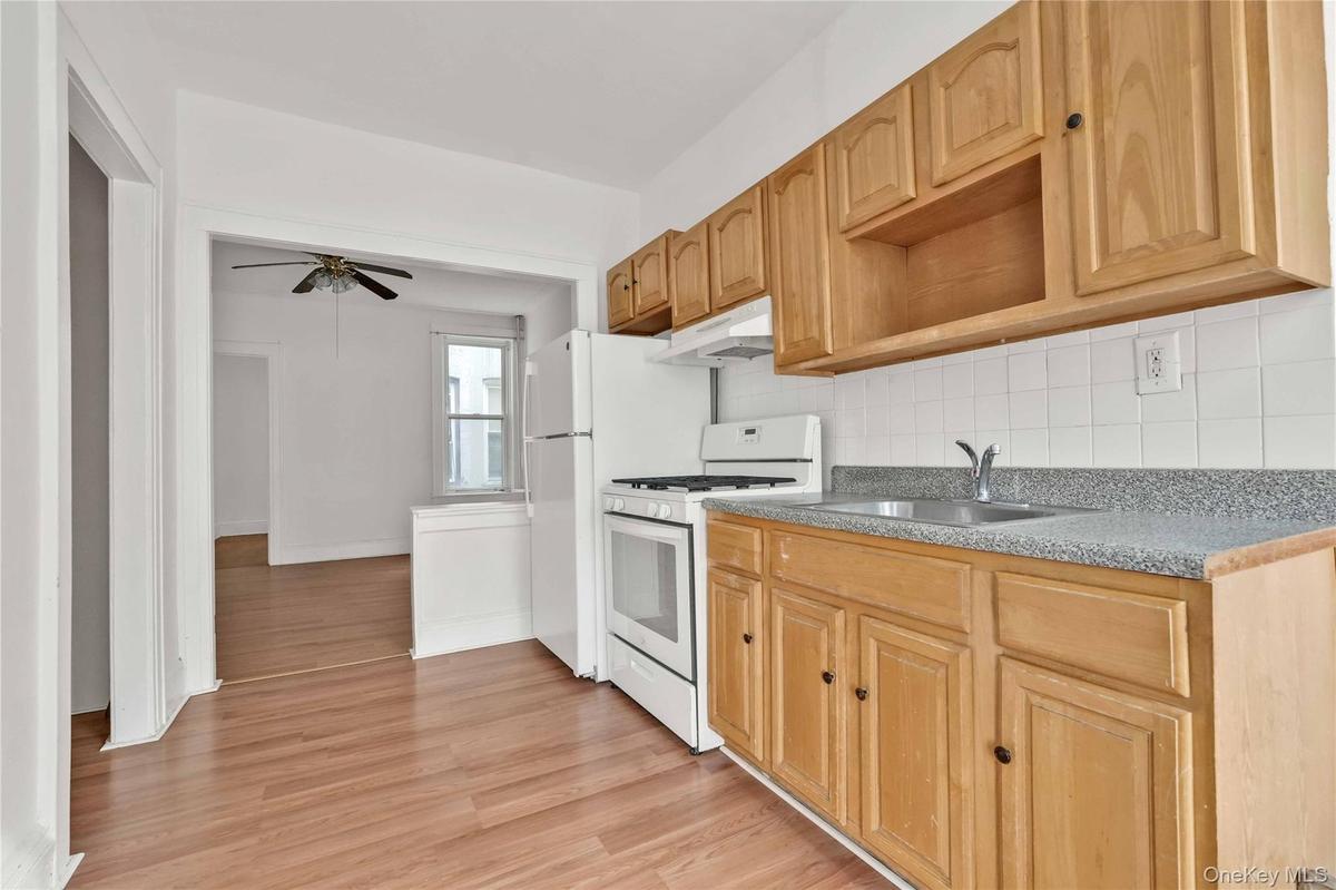 Kitchen featuring white range with gas cooktop, decorative backsplash, light wood-style flooring, under cabinet range hood, and a ceiling fan
