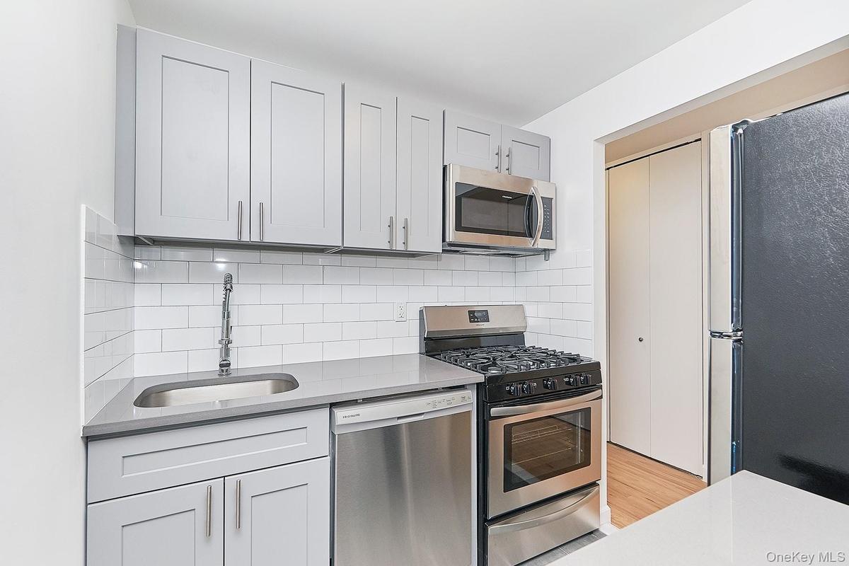 Kitchen with stainless steel appliances, backsplash, and light stone counters